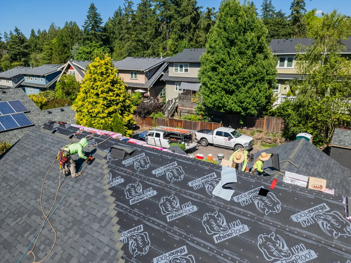 Roofing crew installing shingles and underlayment on a residential roof